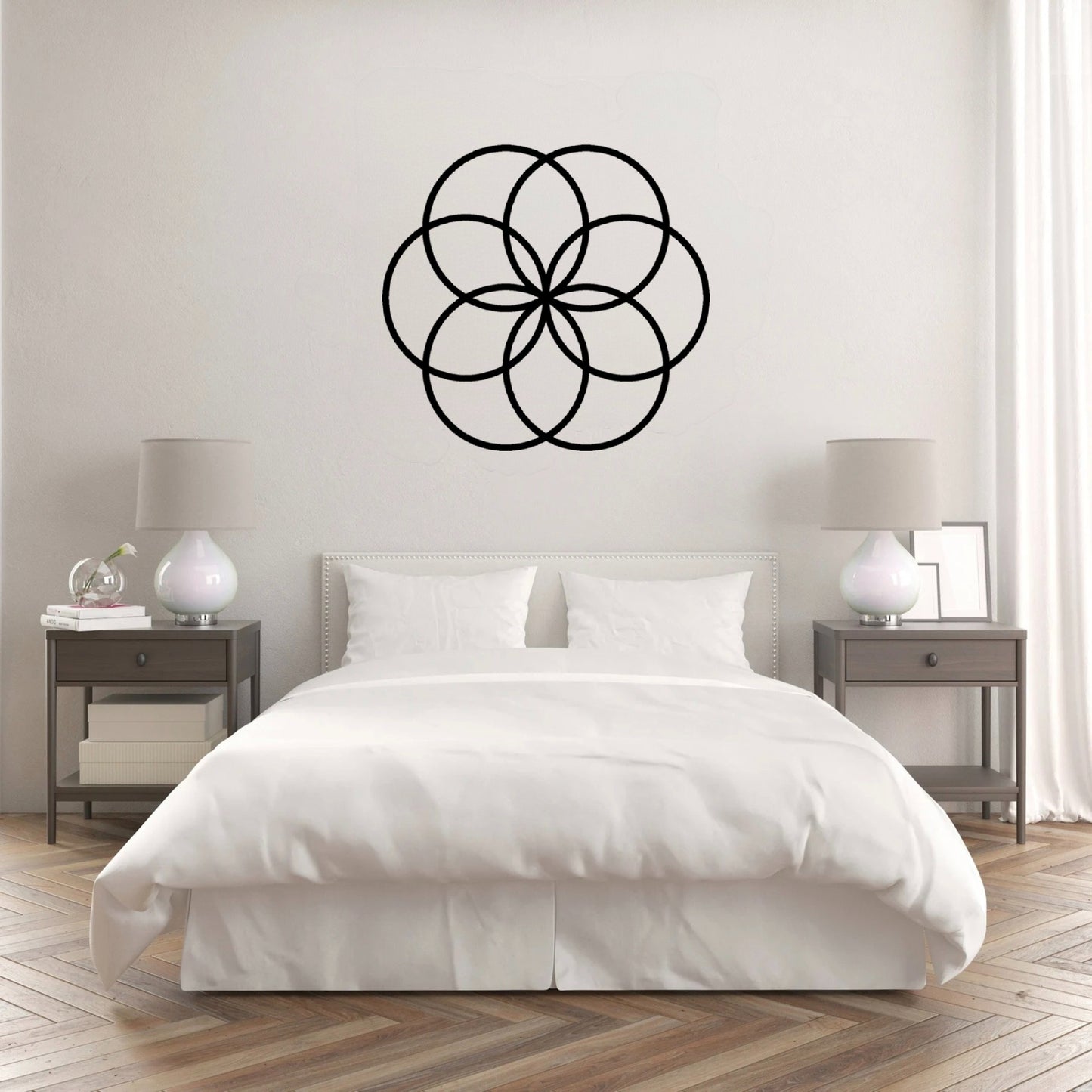 The Cerelia Metal Circles Wall Decor is gracefully hung on the wall above a pristine white bed, creating a visually stunning contrast. The interconnected circles, add a modern, geometric touch that complements the minimalist and clean aesthetic of the room.
