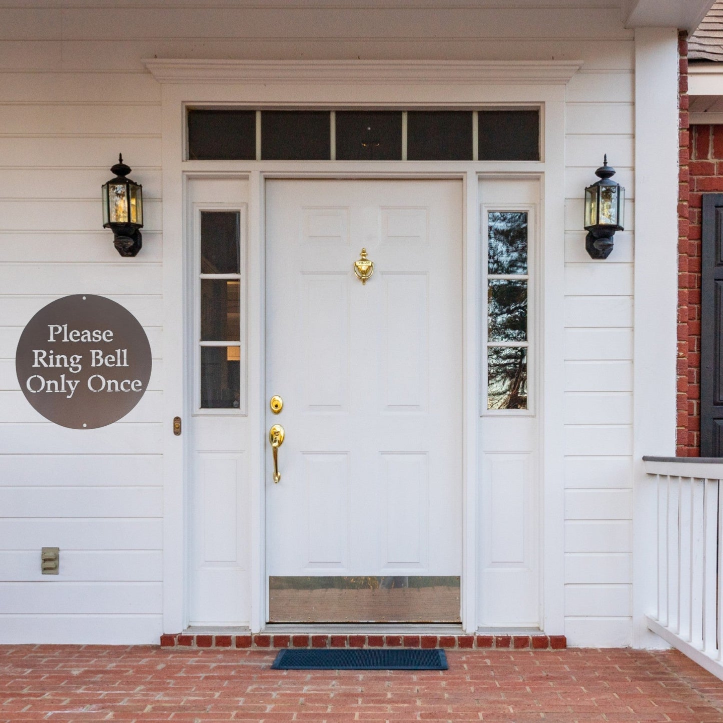 Front door of a white house with an aged copper painted custom metal sign on the wall next to the door