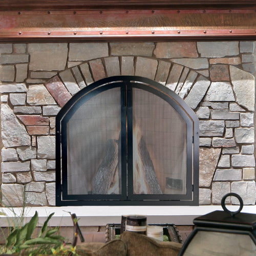 Stone fireplace with an arched metal fireplace screen featuring doors, adding both style and functionality to the rustic hearth setting