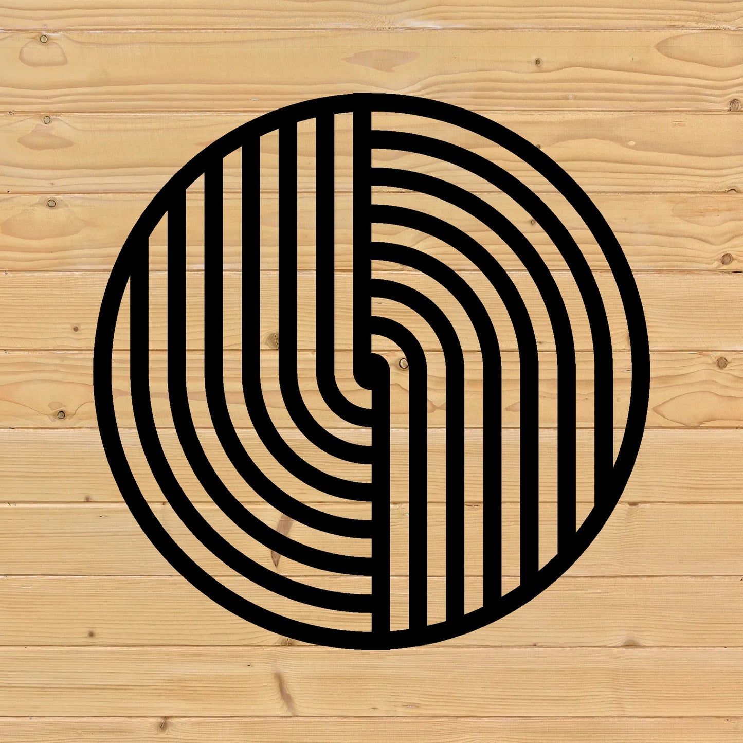 The image showcases a round metal wall art piece with a bold black geometric pattern, mounted on a light wooden fence background. The clean lines of the artwork contrast with the natural wood grain and knots, creating a harmonious blend of modern and rustic aesthetics.