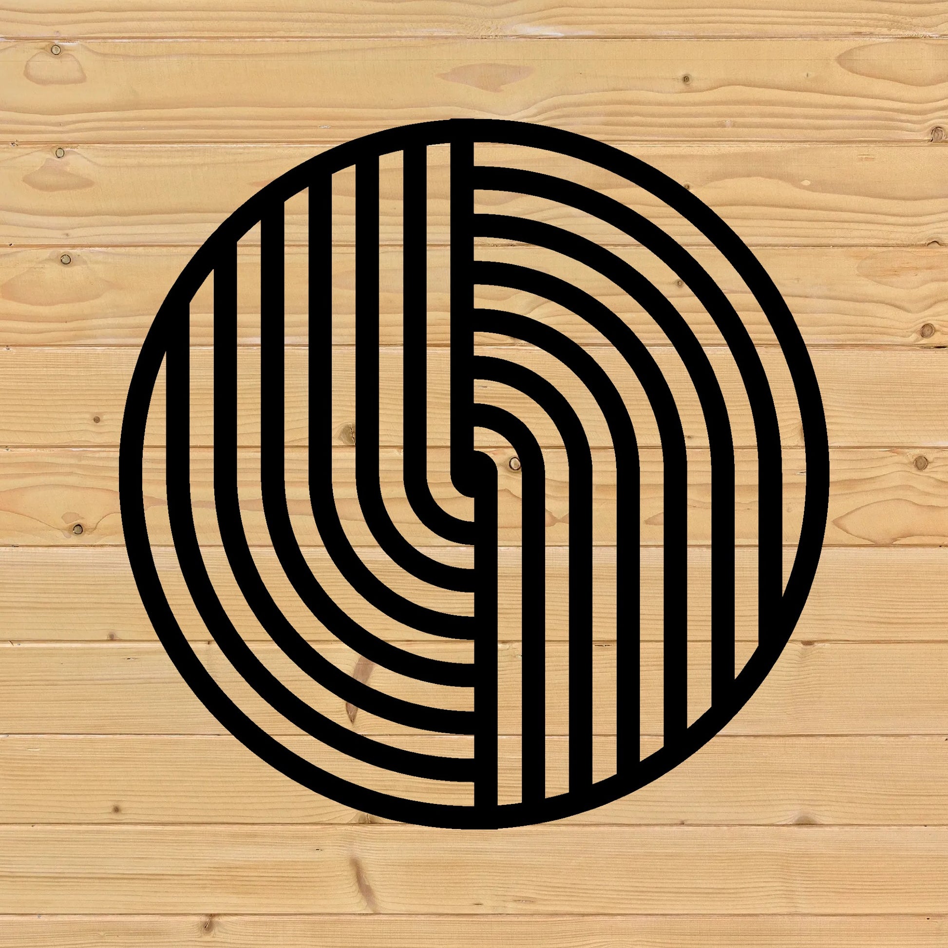 The image showcases a round metal wall art piece with a bold black geometric pattern, mounted on a light wooden fence background. The clean lines of the artwork contrast with the natural wood grain and knots, creating a harmonious blend of modern and rustic aesthetics.