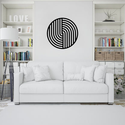 The image showcases a modern living room with a minimalist design. A round metal wall art piece with a bold geometric black pattern hangs above a white sofa, adding a striking contrast to the neutral decor.
