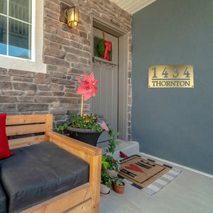 Front porch of a house with a bronze gold home address sign on the wall