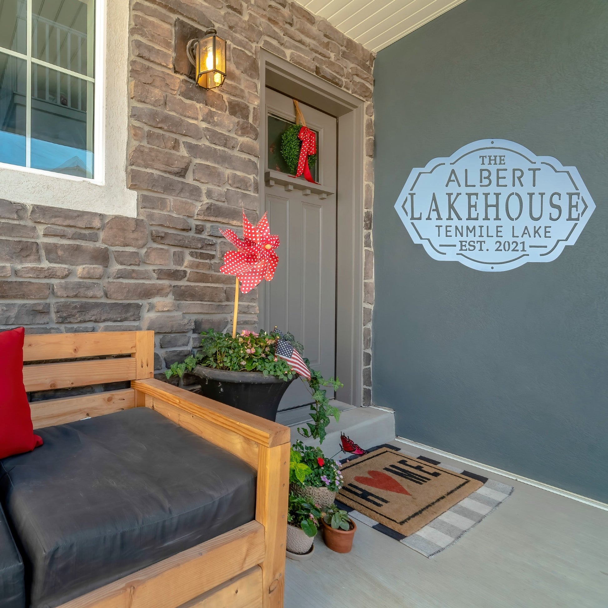 A white lake house sign on the wall outside of a front door on a patio
