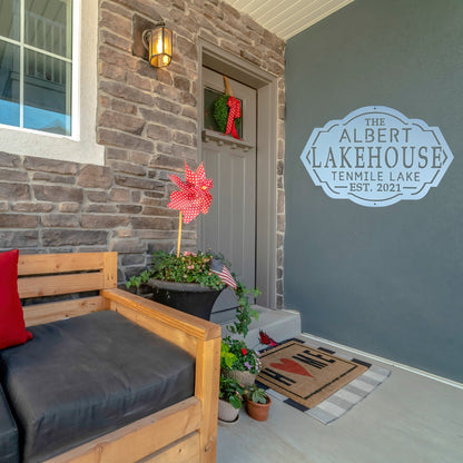 A white lake house sign on the wall outside of a front door on a patio