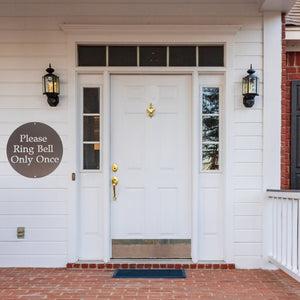 Front door of a white house with an aged copper painted custom metal sign on the wall next to the door 