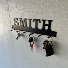 Load image into Gallery viewer, custom family name key rack with family name and mounted on the wall with keys on it