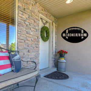 Front porch of a house and next to the front door on the wall there is a custom metal sign in the shape of a football