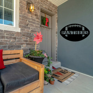 Front porch of a house and on the wall there is a custom metal sign in the shape of a football