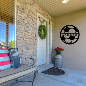 Front porch of a house with a bench and wreath on the door, next to the door is a custom metal sign in the shape of a soccer ball in black paint